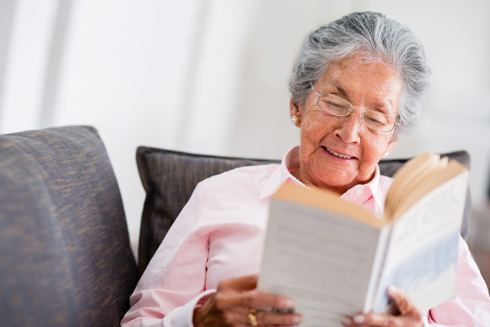 Elder Woman Reading A Book At Home And Smiling